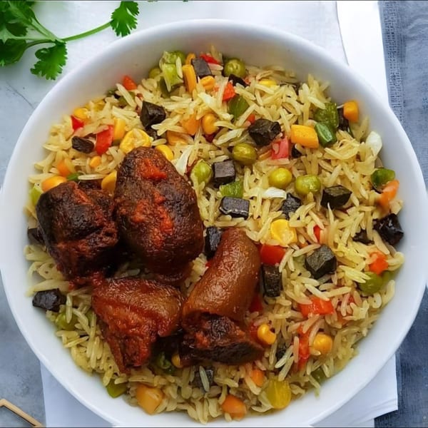 African fried rice with vegetables and three pieces of grilled meat in a white bowl.