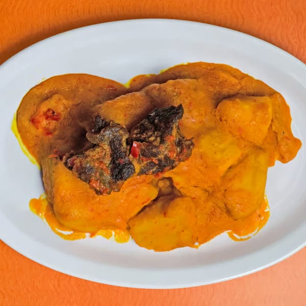 African dish with orange stew and dark meat pieces on a white plate, against an orange background.