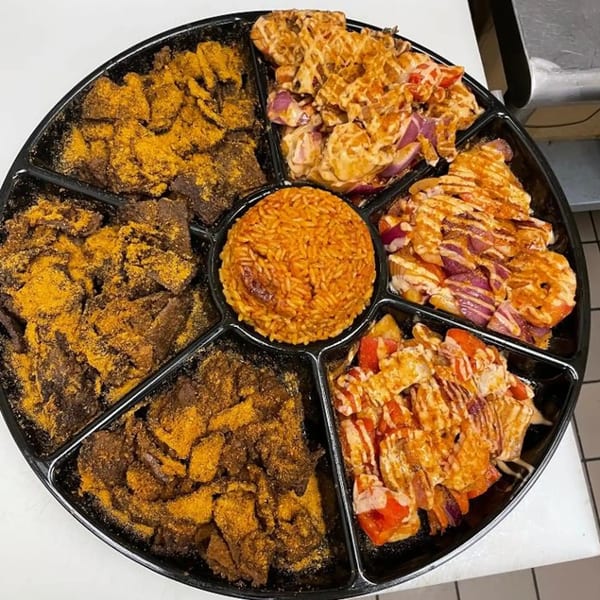 A large black platter from Suya Spot filled with jollof rice, suya, and other African dishes.