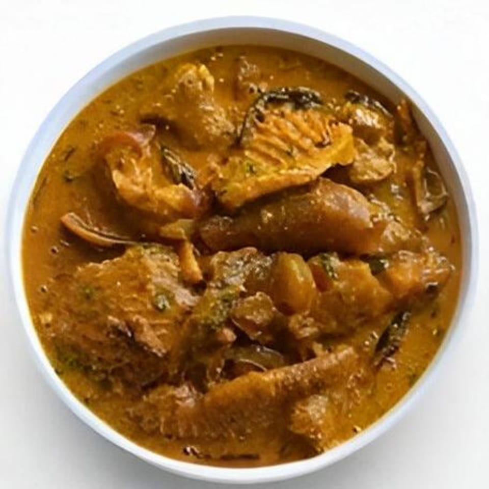 A bowl of rich, orange-brown African soup with various meats and vegetables.