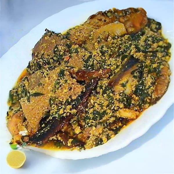 A plate of African stew with meat, green vegetables, and a sprinkle of yellow spice, garnished with lemon.