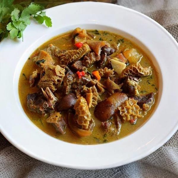 A white bowl filled with a rich, green African soup containing meat and tripe, garnished with cilantro.